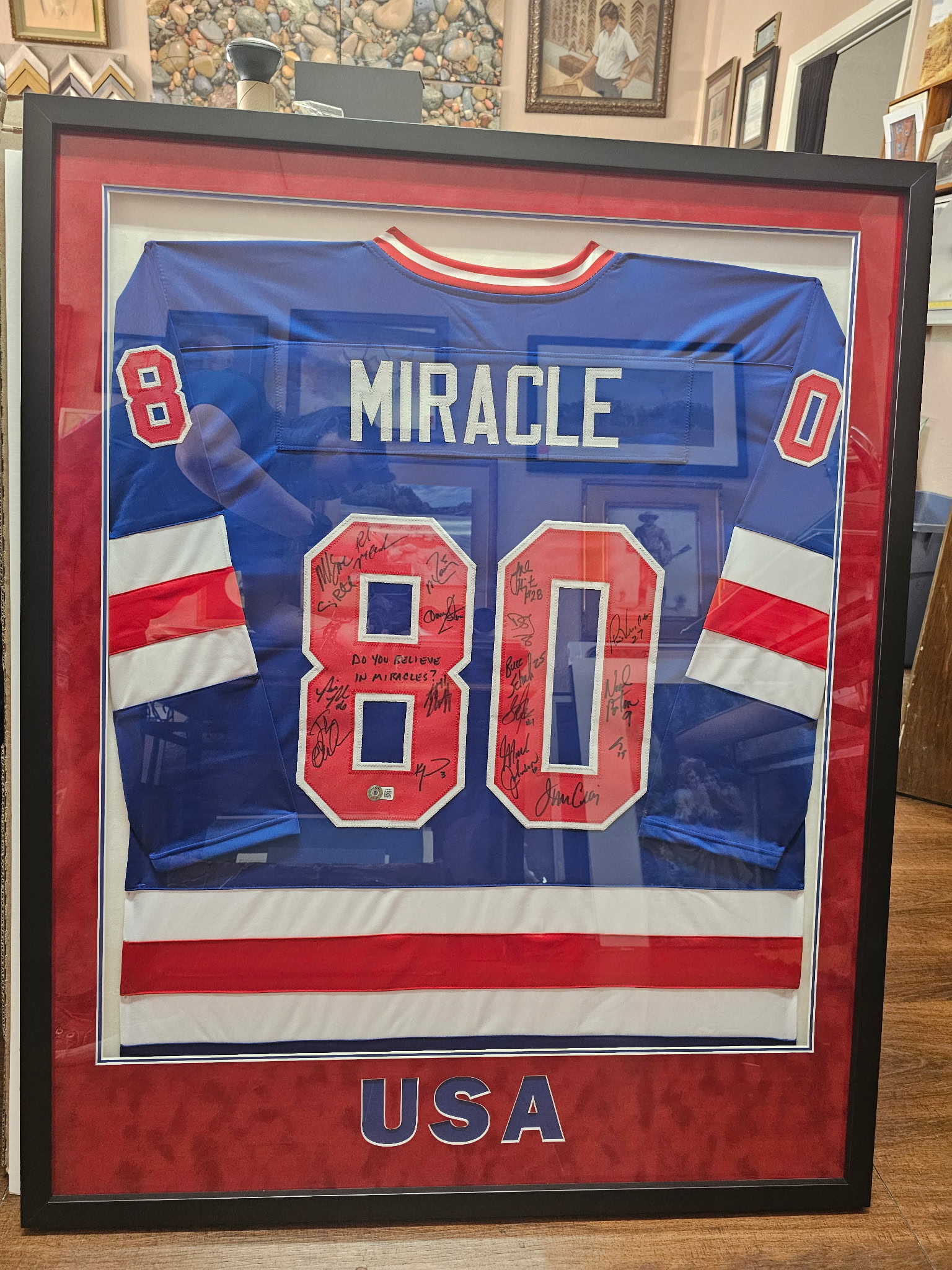 Original phone photo of the 1980 USA Miracle on Ice signed jersey taken in a custom framing shop with background clutter visible